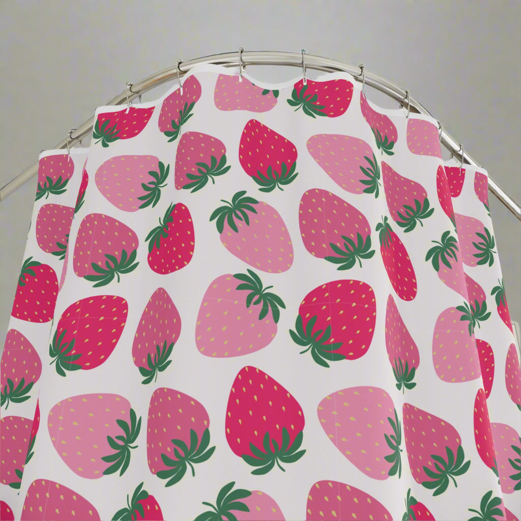 A colorful bathroom shower curtain with a fruit theme, displaying orange and pink fruit patterns against a white background, installed in a bathroom with a plant and a wooden stool in the background.