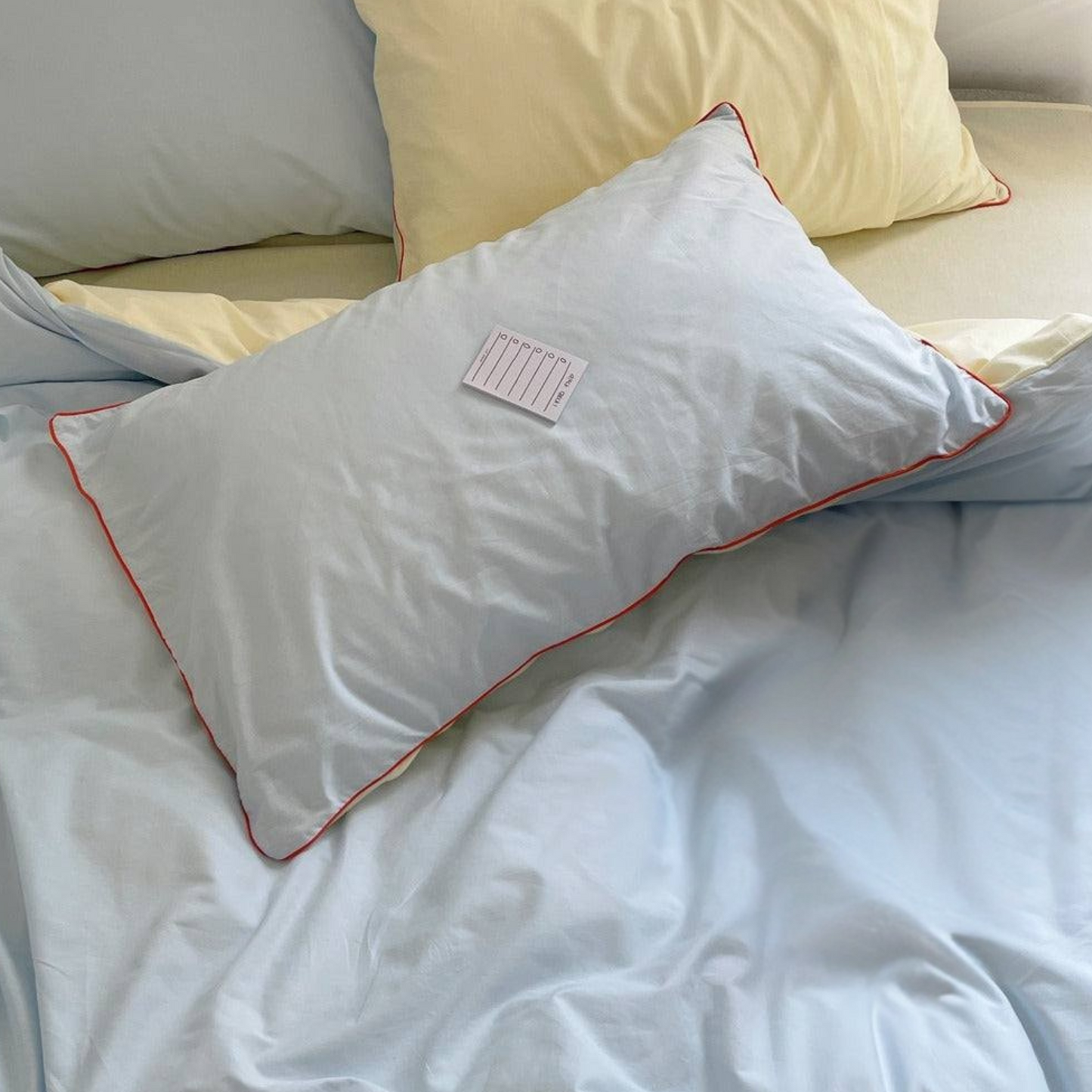 Blue pillow with orange trim on a bed with light-colored pillows and bedding.