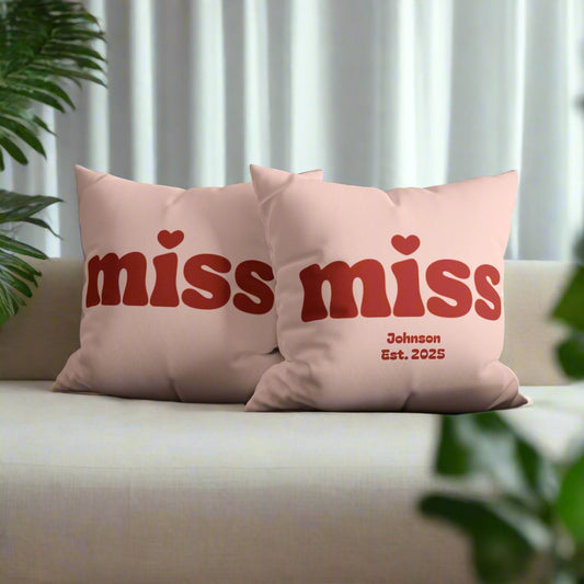 Two pink pillows with 'miss' text on a gray couch.