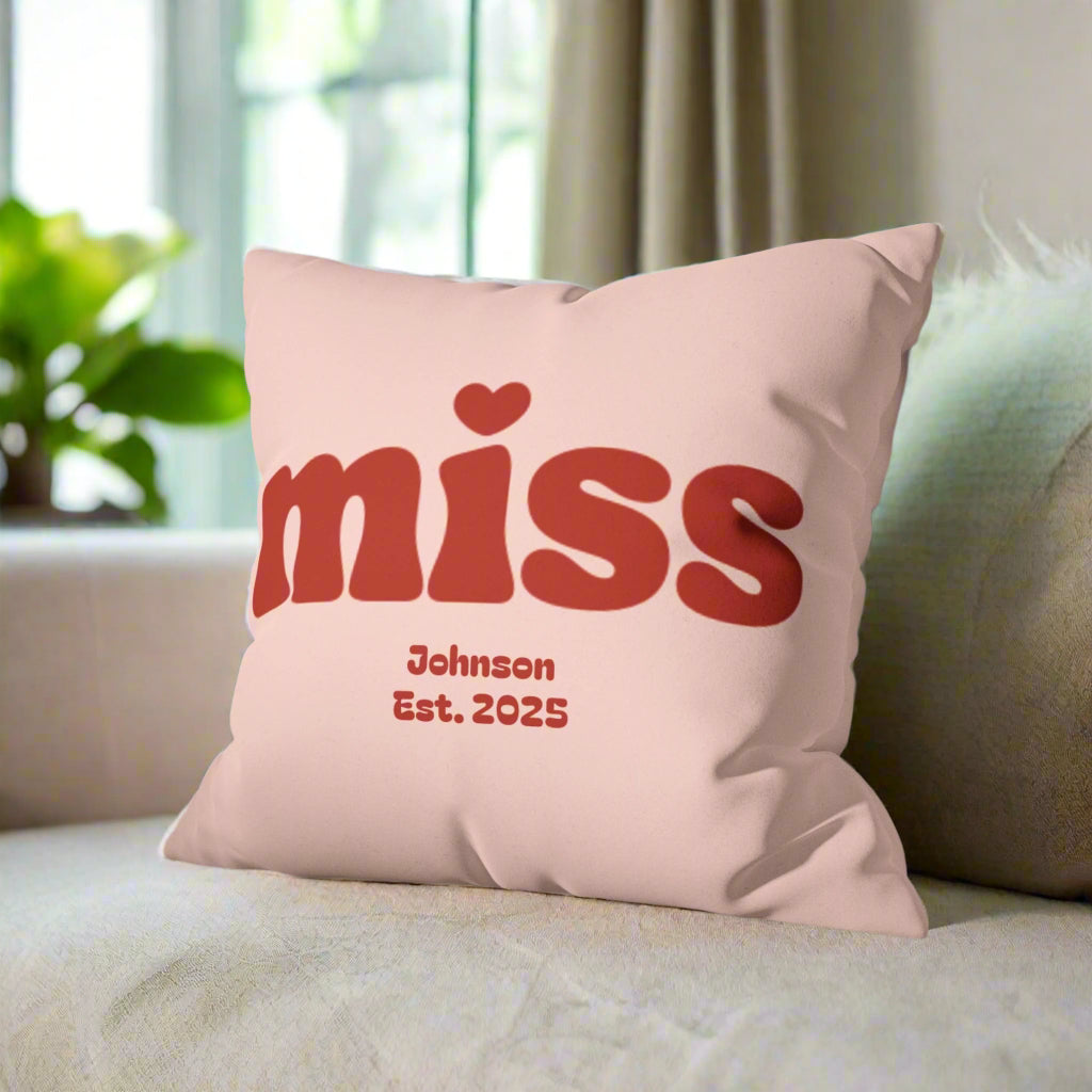 Pink pillow with red text 'miss' and 'Johnson Est. 2025' on a gray couch.