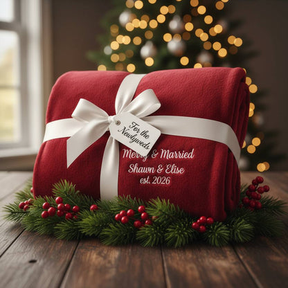 Personalized red Christmas blanket with "Merry & Married" and custom couple names and year, wrapped with white ribbon and holiday greenery.