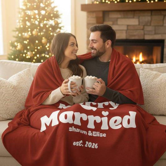 Couple wrapped in personalized Christmas blanket with "Merry Married" and custom names Shawn & Elise est. 2026 in festive living room