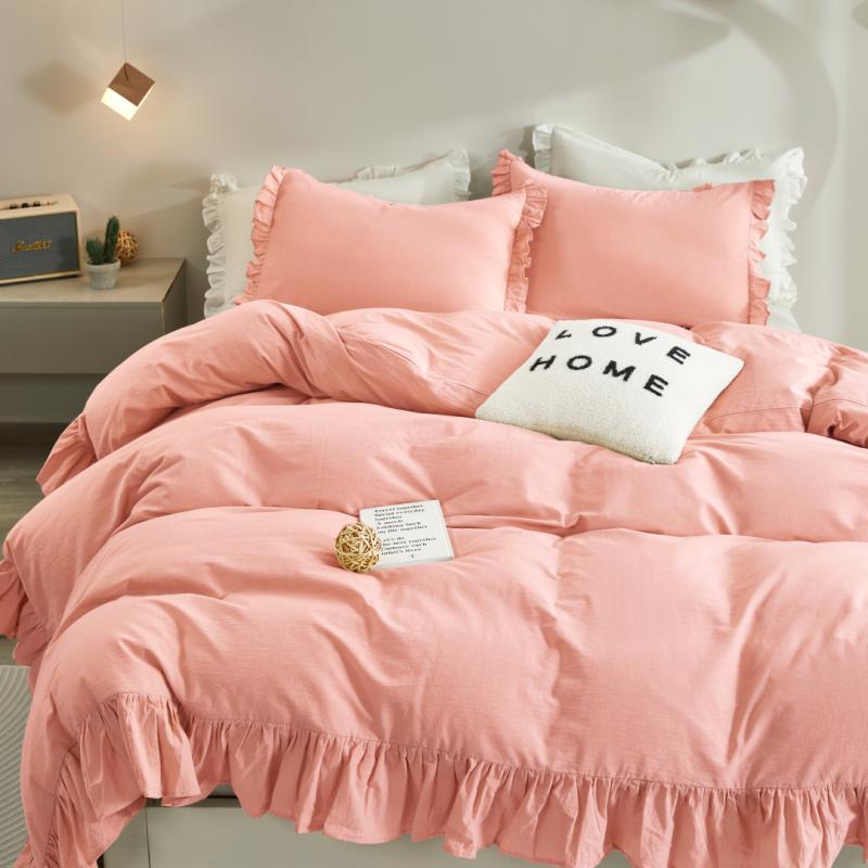 Pink bedding set with ruffled edges on a bed in a bedroom setting.