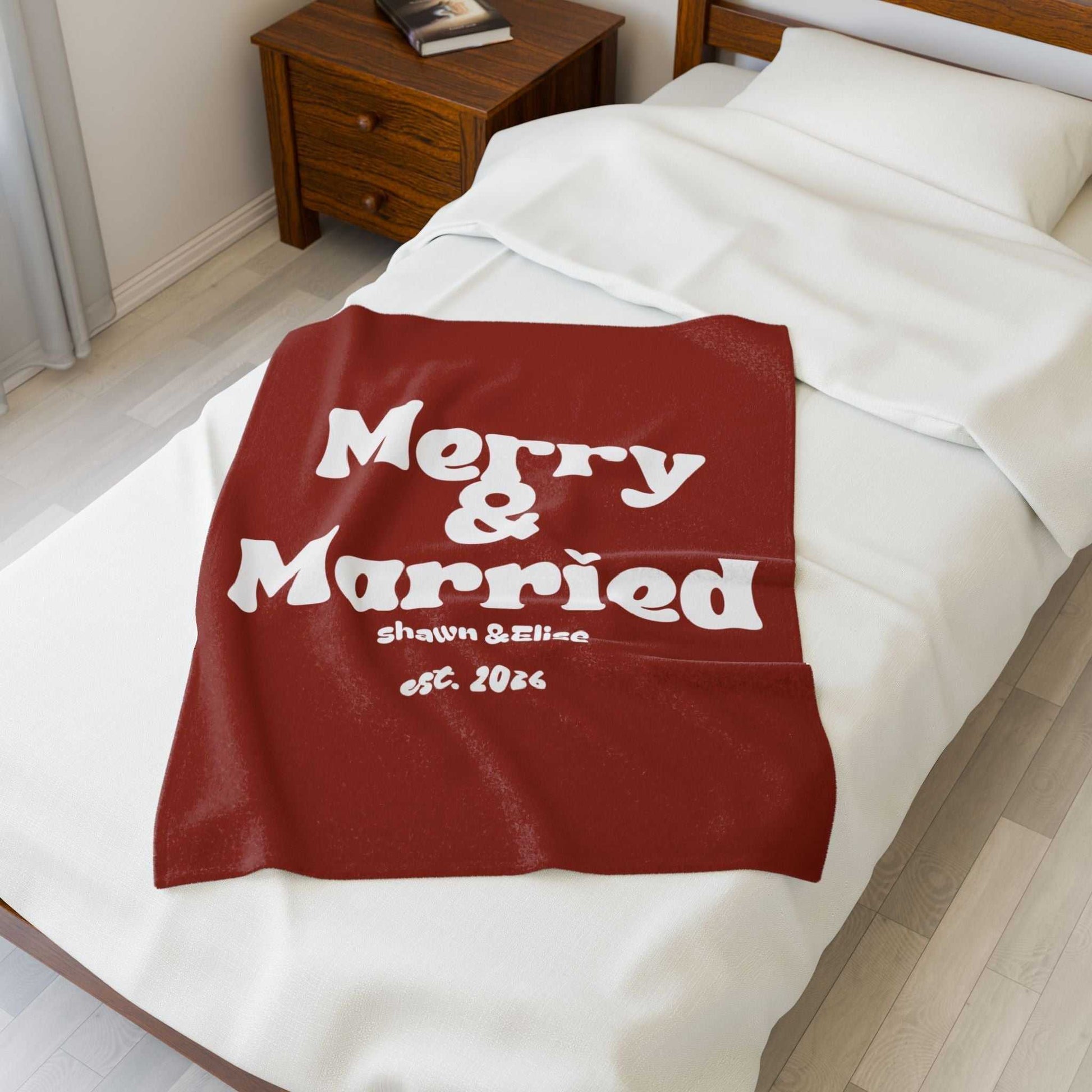 Personalized Christmas blanket in red with white retro "Merry & Married" text, custom names, and established year on bed
