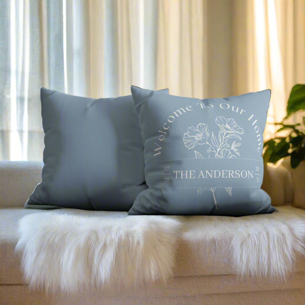 Blue pillow with 'Welcome to Our Home' text on a gray sofa