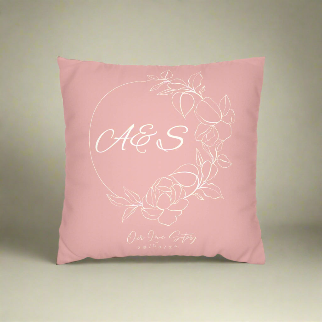 Pink pillow with white floral design and initials on a white background