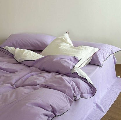  a bed covered with a lilac duvet and white pillows