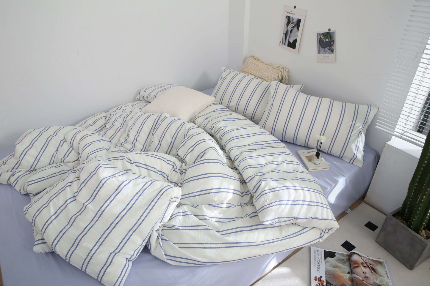 Blue stripe washed cotton bedding set on a bed with pillows and a magazine.