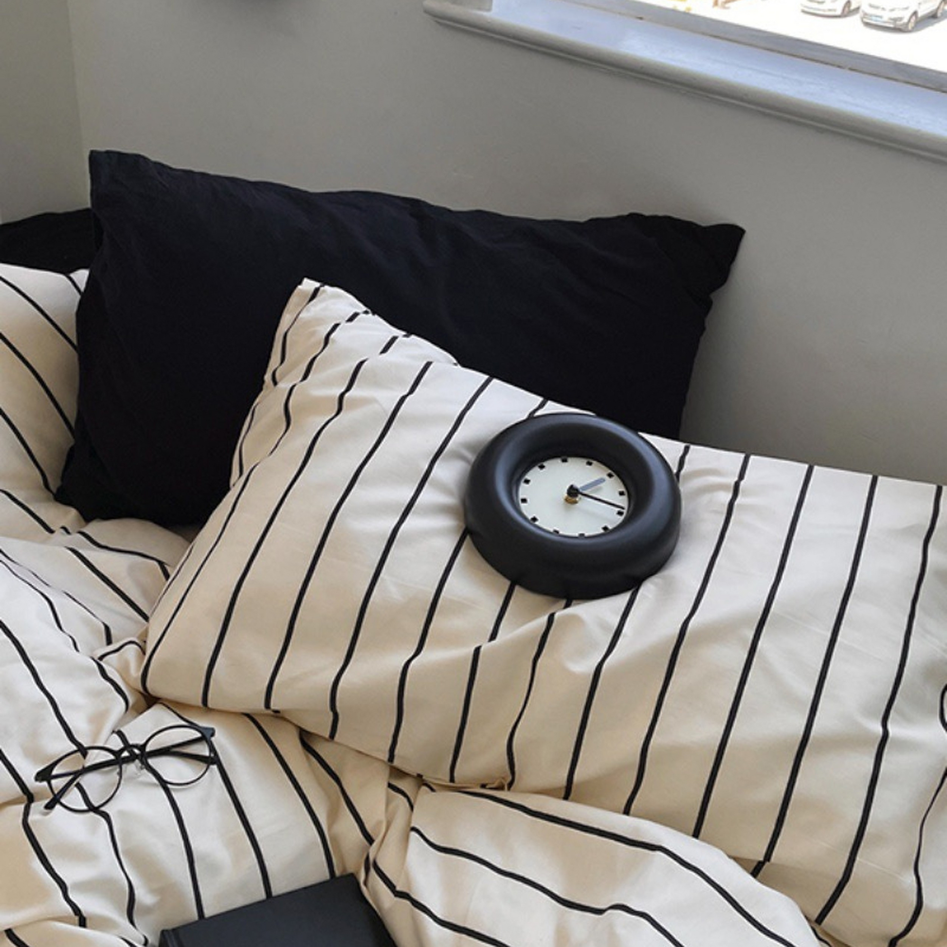 Black and white striped bedding with a small round clock on a bed.
