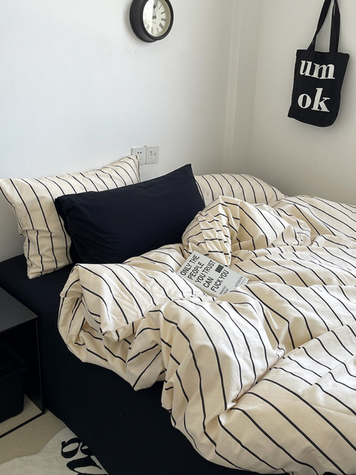 Bed with striped bedding and pillows in a room with a clock and bag on the wall.