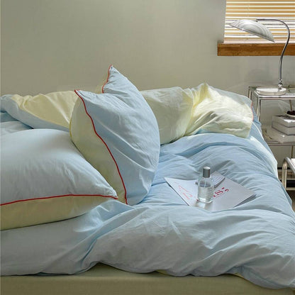 Light blue and crimson bedding set with vibrant piping on a cozy bed.